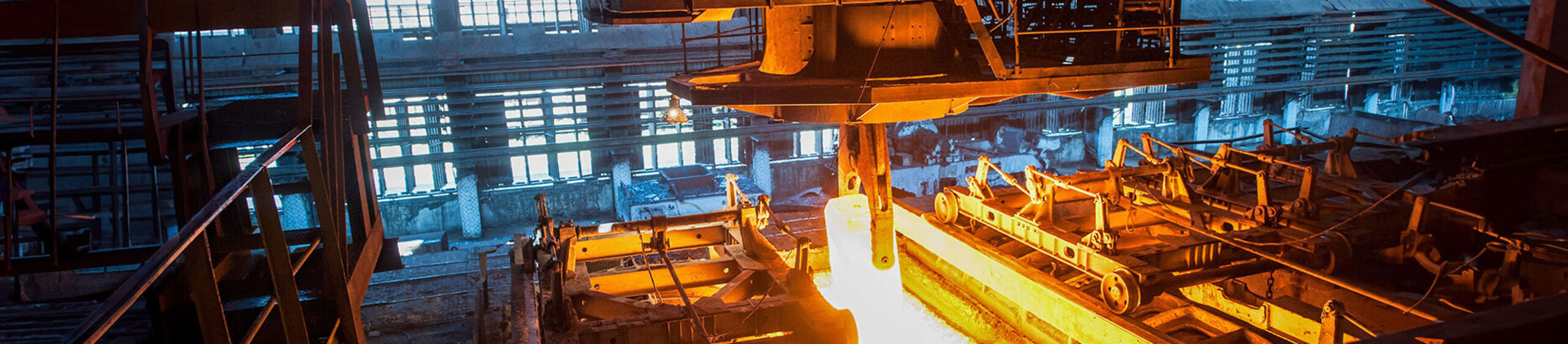 Ein Kran hebt in einem Stahlwerk einen Block glühendes Metall an