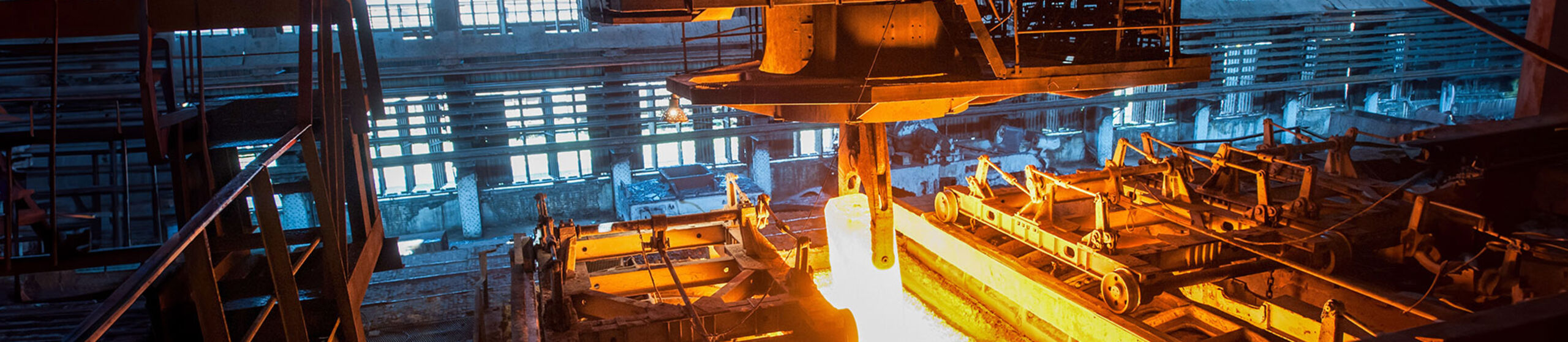 Ein Kran hebt in einem Stahlwerk einen Block glühendes Metall an
