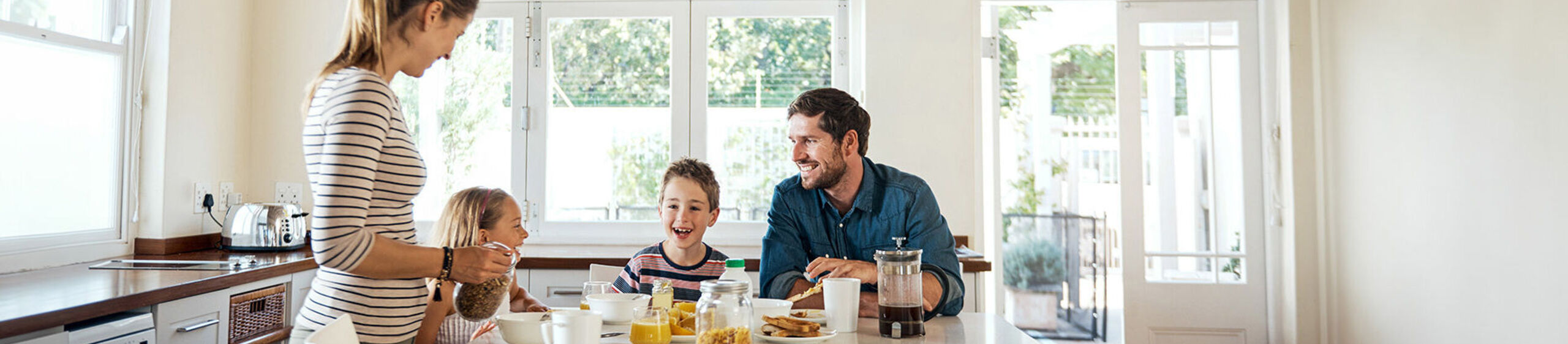 Eine Familie mit 2 Kindern sitzt in einer hellen Küche am Frühstückstisch