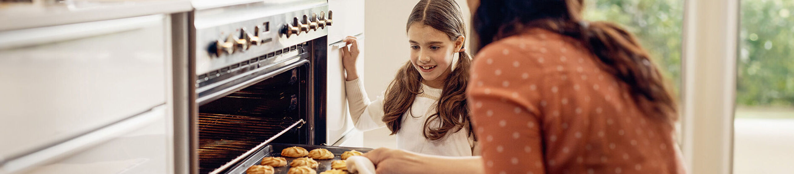 Mutter und Tochter vor einem geöffneten Backofen mit einem Blech voller Plätzchen