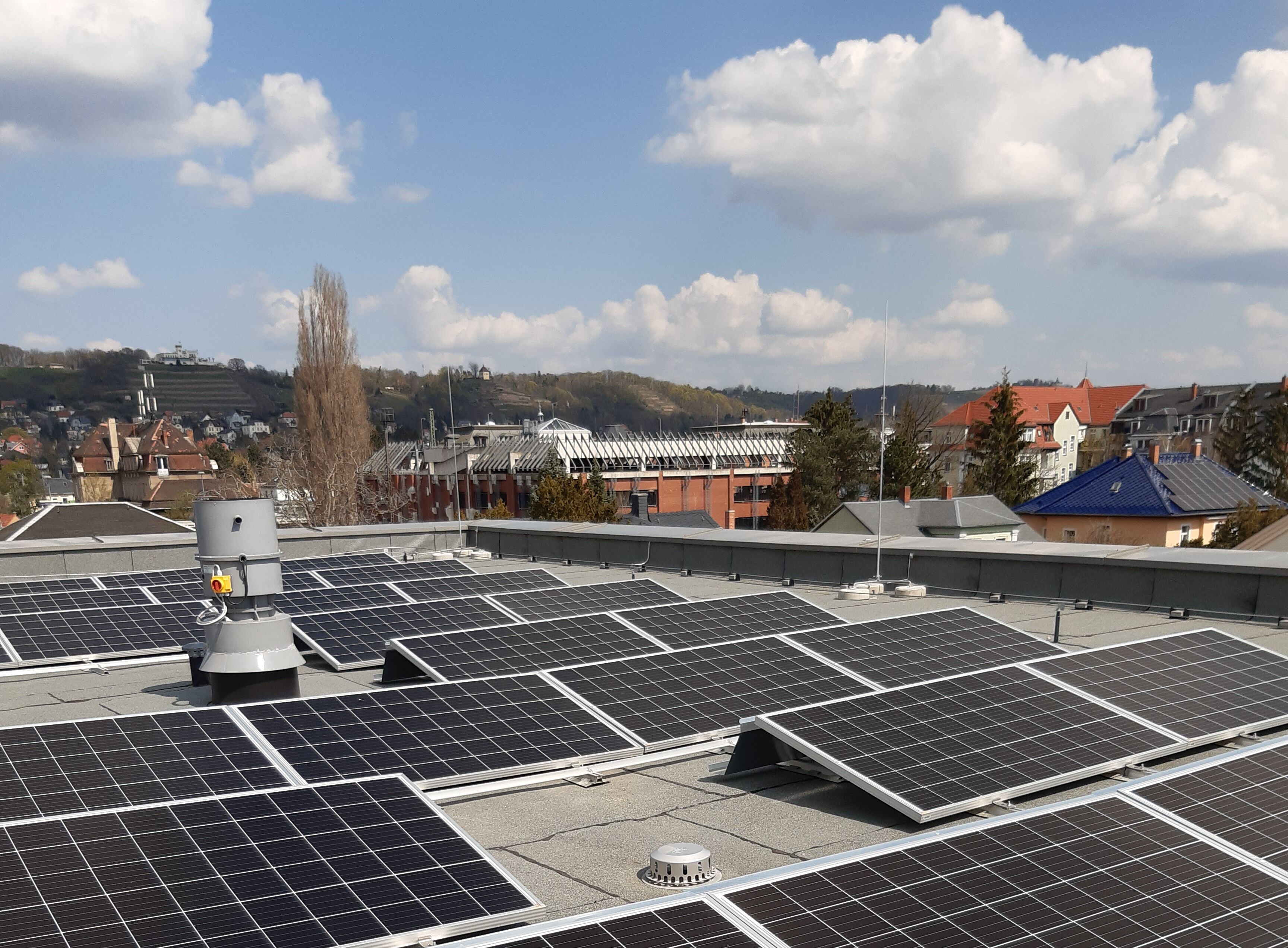 Solarmodule auf einem Dach, im Hintergrund Gebäude