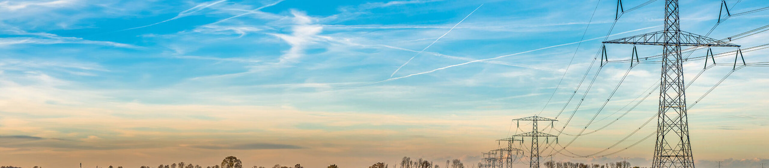 Strommasten auf einem Feld vor blauem Himmel